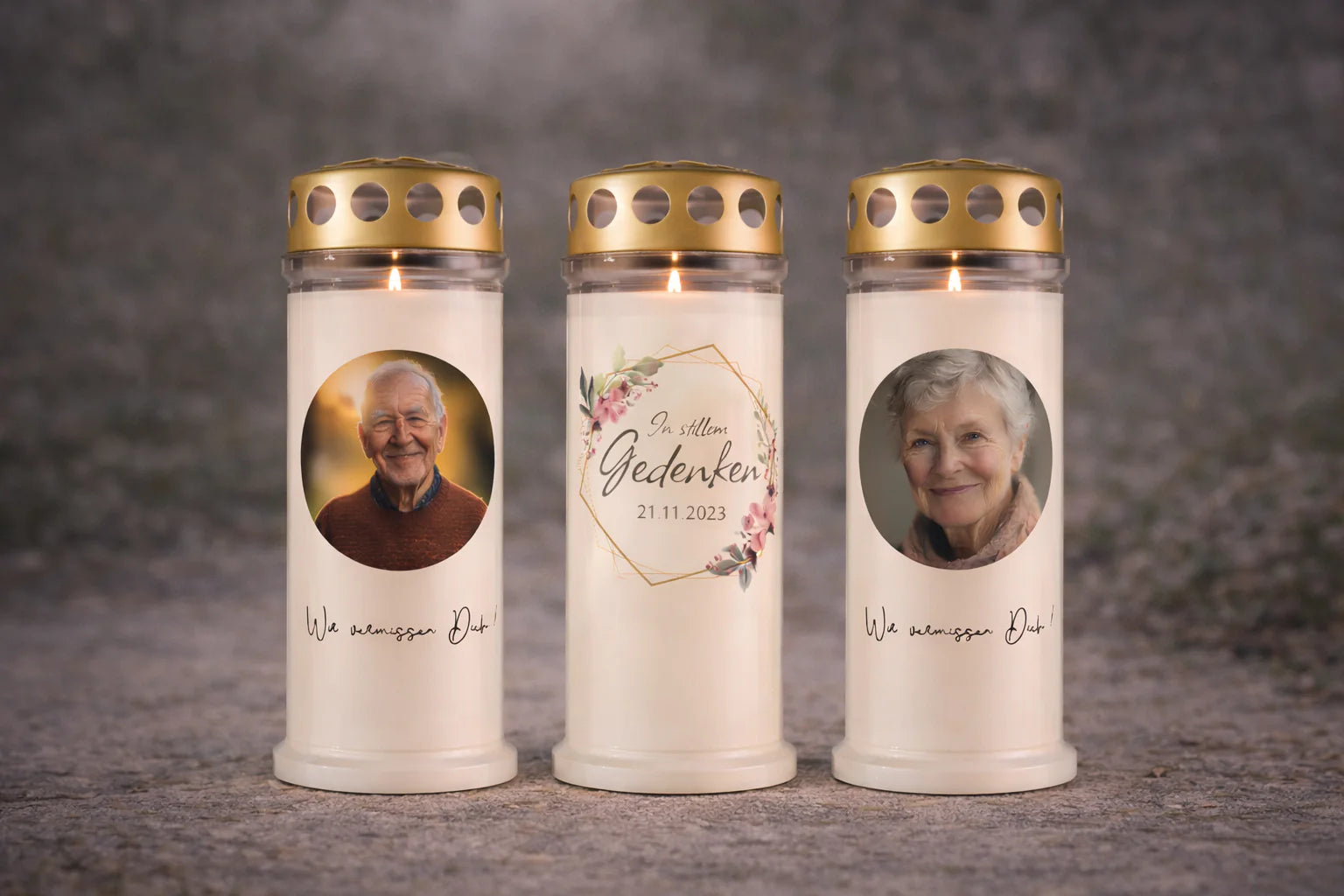 Drei personalisierte Grablichter mit Golddeckel und sichtbarer Flamme, mittig „In stillem Gedenken“, daneben zwei Fotokerzen mit Porträts, vor ruhigem, neutralem Hintergrund