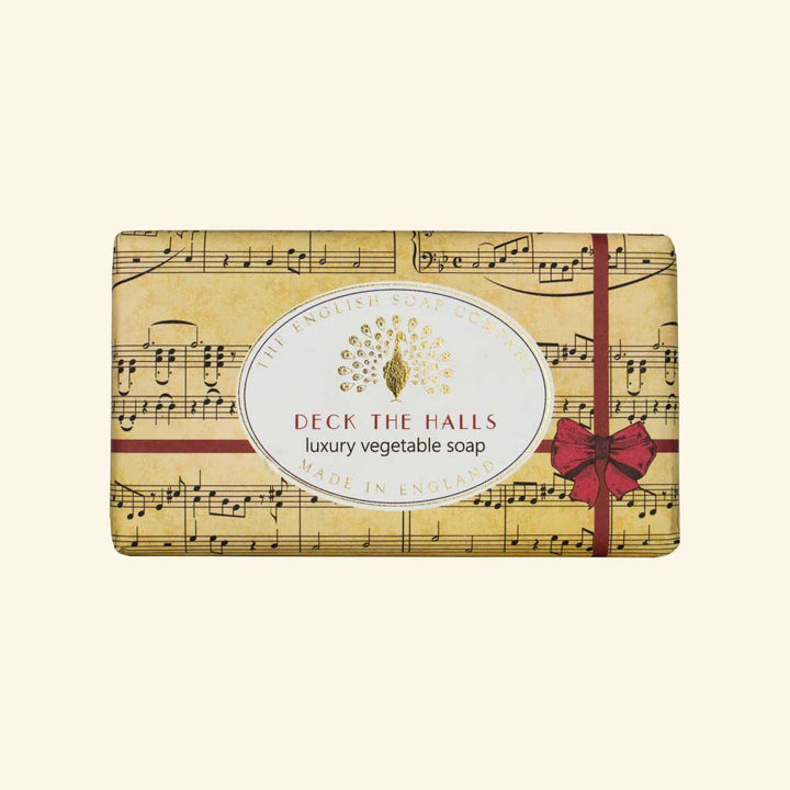 “Beige Seife mit Notenblatt-Design, roter Schleife und Aufschrift ‘Deck the Halls – luxury vegetable soap’.”
