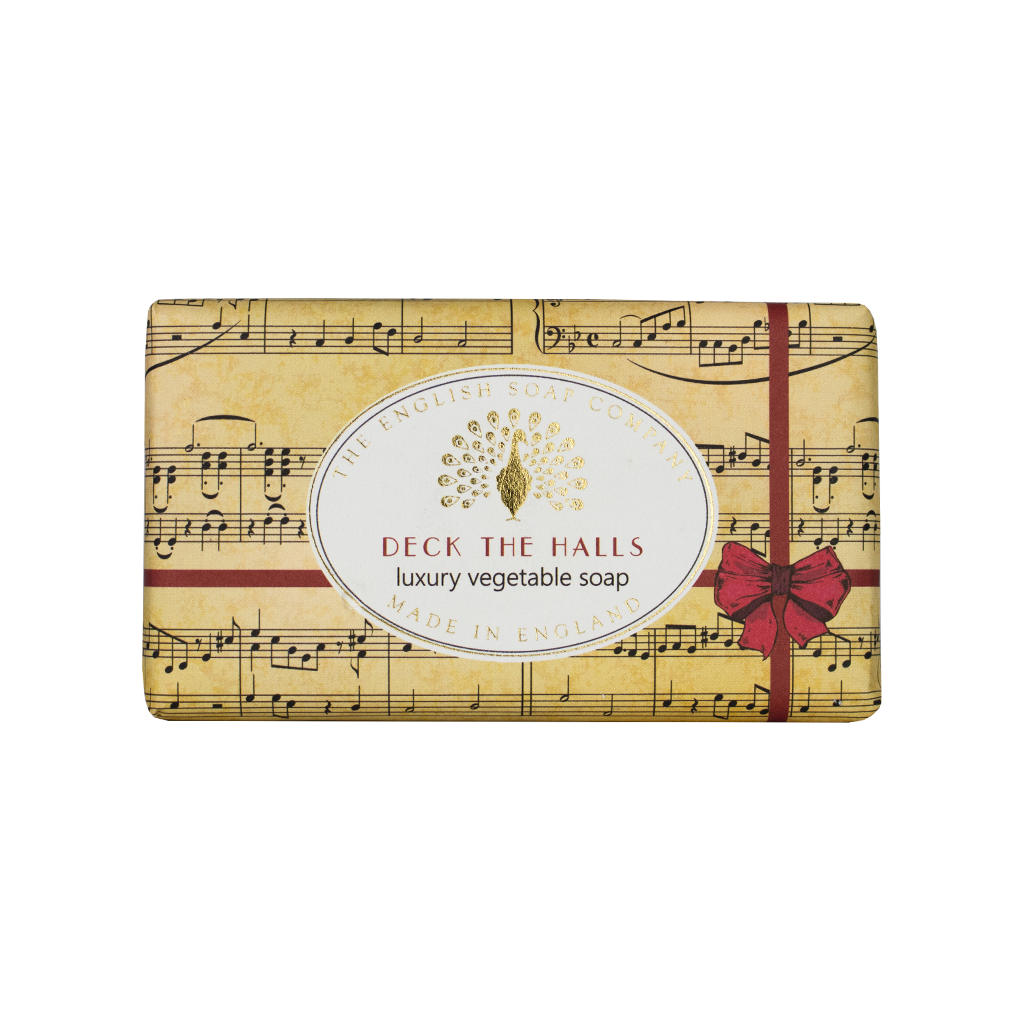 “Beige Seife mit Notenblatt-Design, rotem Geschenkband und Aufschrift ‘Deck the Halls – luxury vegetable soap’.”