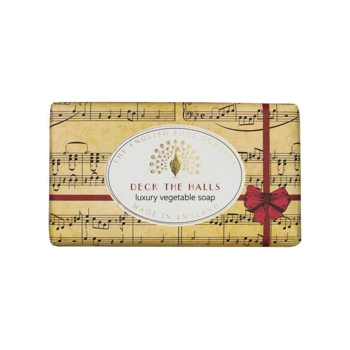 “Beige Seife mit Notenblatt-Design, rotem Geschenkband und Aufschrift ‘Deck the Halls – luxury vegetable soap’.”