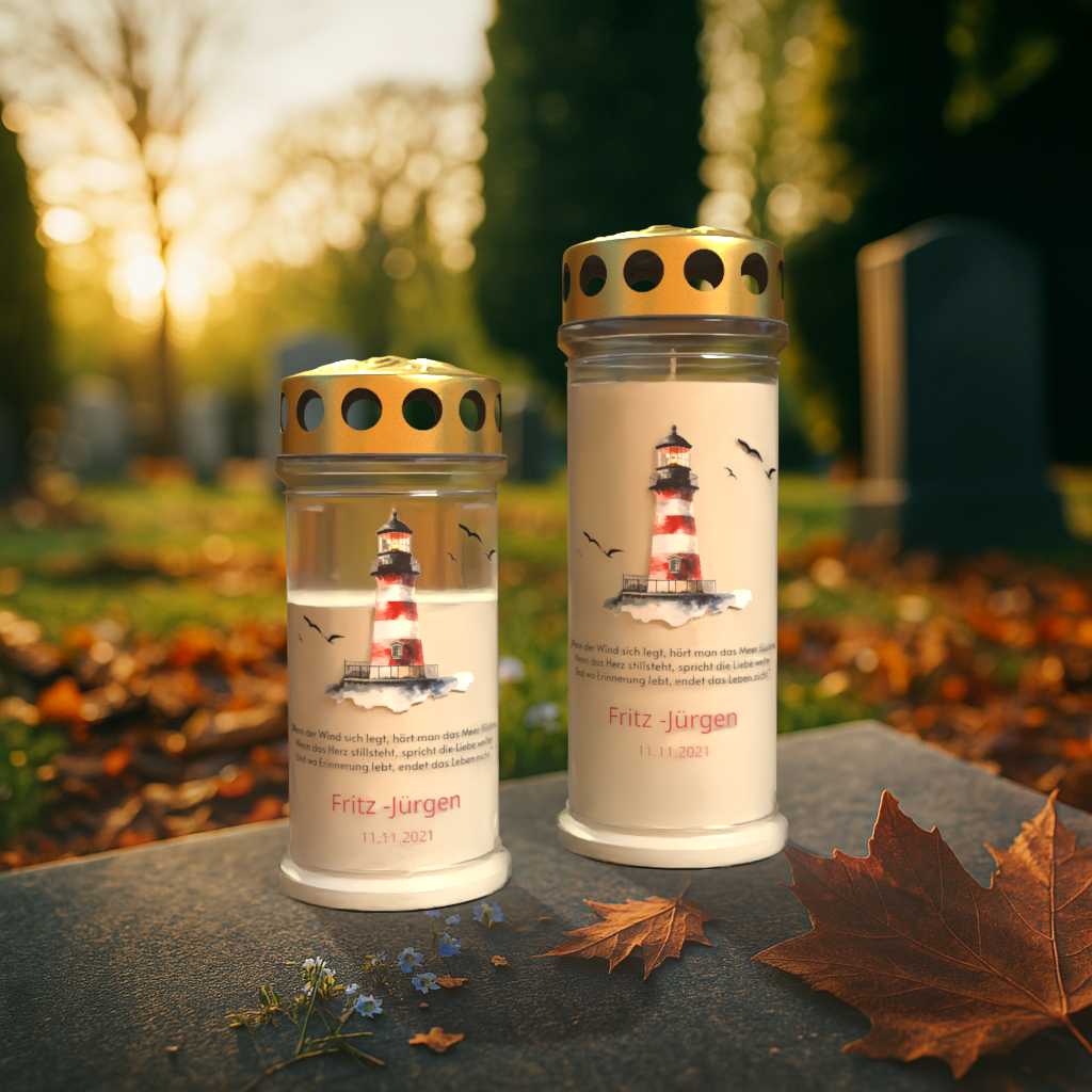 Zwei Gedenkkerzen mit goldenen Deckeln stehen auf einem Grabstein bei herbstlichem Sonnenuntergang auf einem Friedhof. Beide Kerzen zeigen ein maritimes Motiv mit einem rot-weiß gestreiften Leuchtturm, umgeben von Möwen, sowie den Namen „Fritz - Jürgen“ und das Datum „11.11.2021“. Darunter steht ein poetischer Spruch über Erinnerung und das Meer. Im Vordergrund liegen Herbstblätter und kleine blaue Blumen, im Hintergrund sind Grabsteine und Bäume im warmen Licht sichtbar.