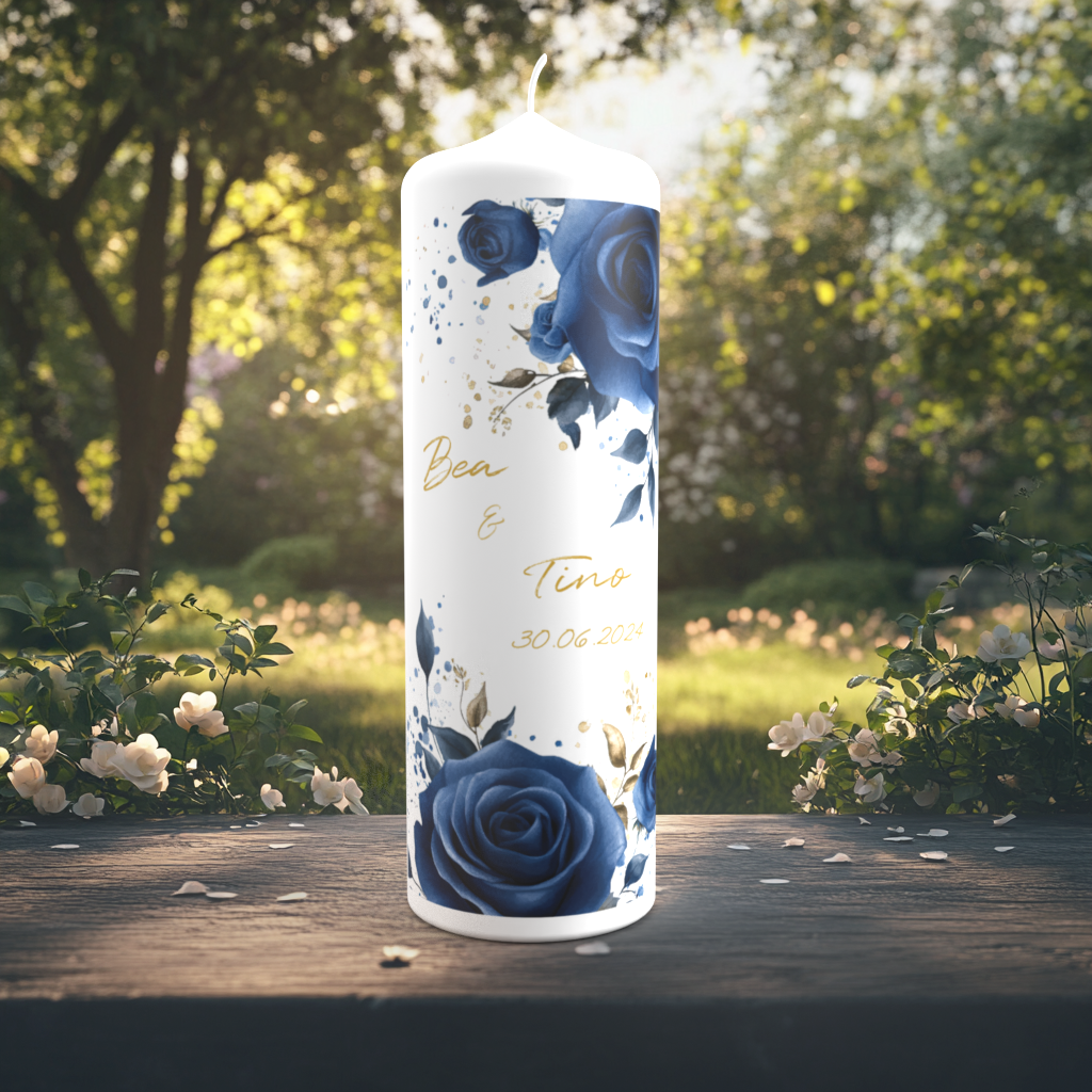 Eine festlich gestaltete Hochzeitskerze steht auf einem Holztisch in einem sonnigen Garten mit weiß blühenden Sträuchern im Hintergrund. Die Kerze ist mit kräftigen dunkelblauen Rosen, goldenen Akzenten und Farbklecksen dekoriert. In der Mitte stehen die Namen „Bea & Tino“ in goldener Schreibschrift sowie das Hochzeitsdatum „30.06.2024“. Das Design wirkt modern, elegant und kontrastreich.