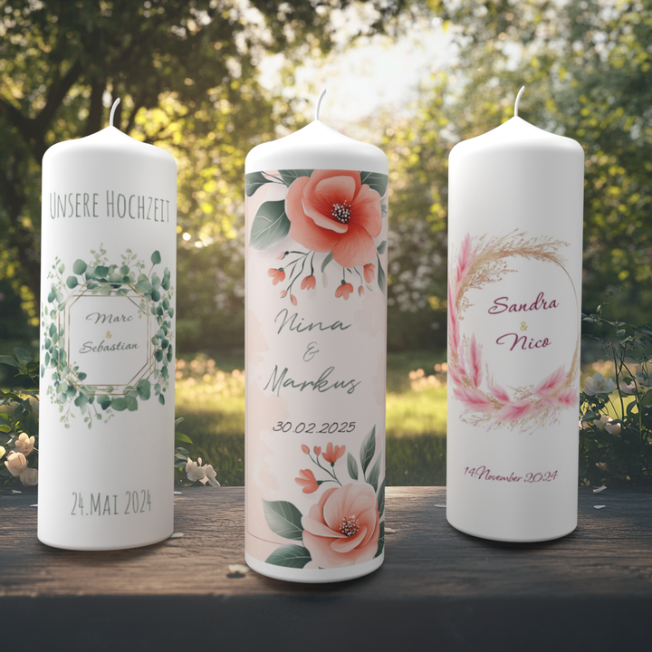Drei individuell gestaltete Hochzeitskerzen stehen nebeneinander auf einer Holzfläche im Grünen bei Sonnenlicht.
	•	Die linke Kerze zeigt ein Eukalyptus-Design mit der Aufschrift „UNSERE HOCHZEIT“ sowie den Namen „Marc & Sebastian“ und das Datum „24. Mai 2024“.
	•	Die mittlere Kerze trägt große Blüten in Rosa und Koralle, dazu die Namen „Nina & Markus“ und das (fiktive) Datum „30.02.2025“.
	•	Die rechte Kerze ist mit rosa Gräsern und floraler Girlande geschmückt. Darauf stehen die Namen „Sandra & Nico“ sowi