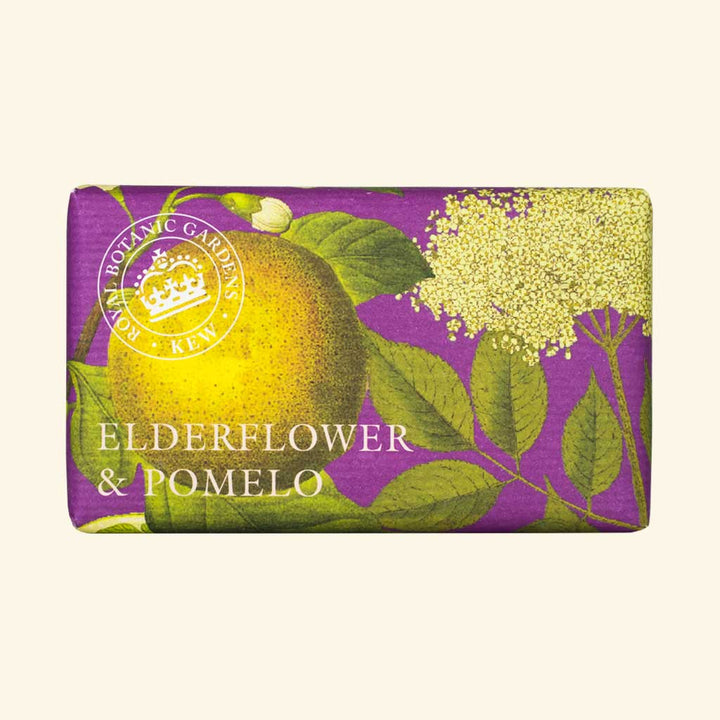 “Seife in edlem Papier mit Illustration von Holunderblüten und Pomelo auf violettem Hintergrund, Text: Elderflower & Pomelo.”