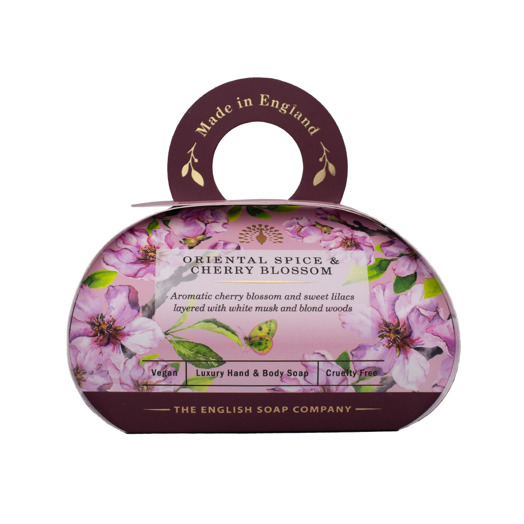 „Luxus-Hand- und Körperseife der Marke The English Soap Company in ovaler Verpackung mit Tragegriff, Motiv: Kirschblüten, Flieder und Blätter auf dunklem Hintergrund, Aufschrift: ‚Oriental Spice & Cherry Blossom – Aromatic cherry blossom and sweet lilacs layered with white musk and blond woods‘.“