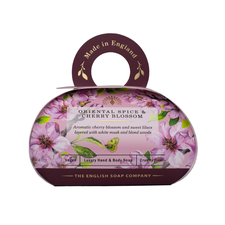 „Luxus-Hand- und Körperseife der Marke The English Soap Company in ovaler Verpackung mit Tragegriff, Motiv: Kirschblüten, Flieder und Blätter auf dunklem Hintergrund, Aufschrift: ‚Oriental Spice & Cherry Blossom – Aromatic cherry blossom and sweet lilacs layered with white musk and blond woods‘.“