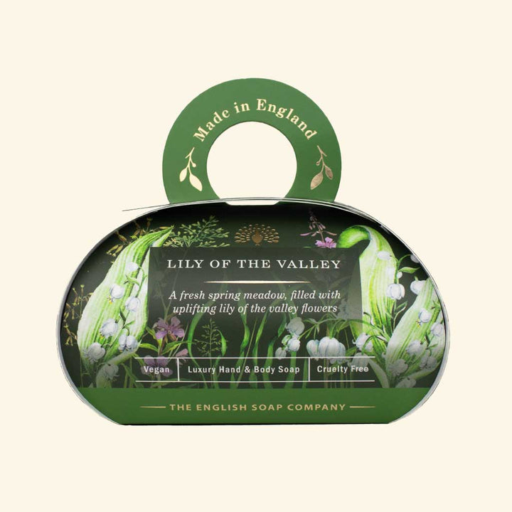 „Luxus-Hand- und Körperseife der Marke The English Soap Company in ovaler Verpackung mit Tragegriff, Motiv: Maiglöckchen und Frühlingsblumen auf dunklem Hintergrund, Aufschrift: ‚Lily of the Valley – A fresh spring meadow, filled with uplifting lily of the valley flowers‘.“