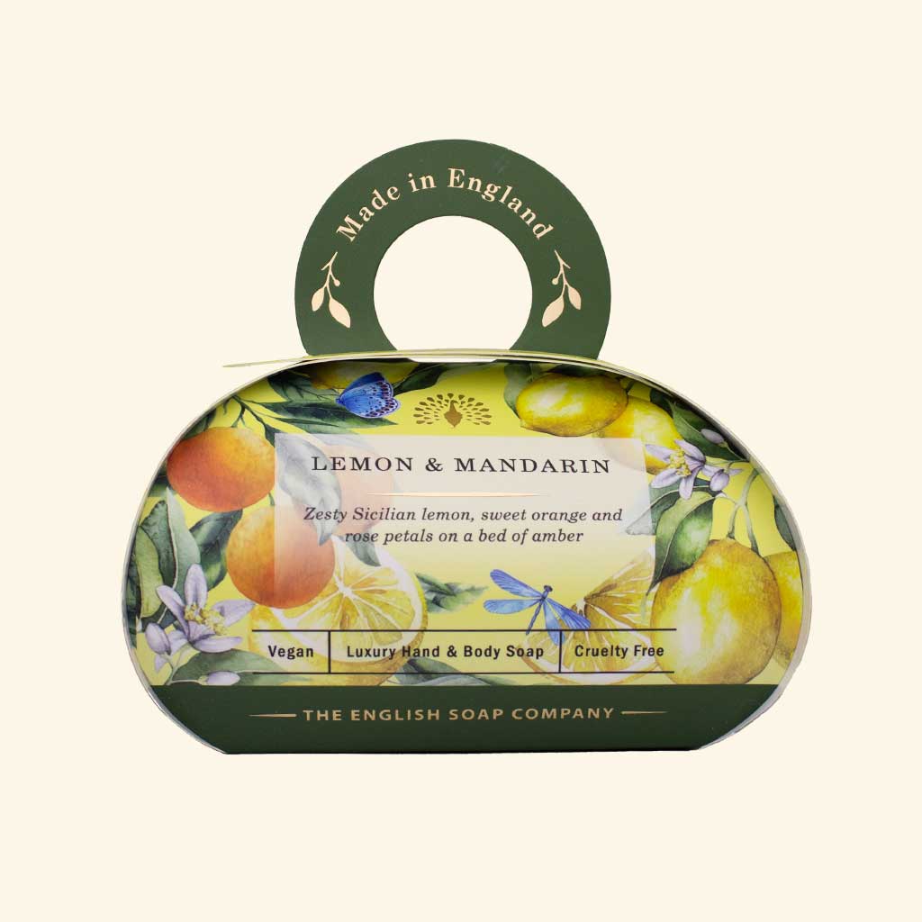 Luxus-Hand- und Körperseife der Marke The English Soap Company in ovaler Verpackung mit Tragegriff, Motiv: Zitronen, Mandarinen und Blüten, Aufschrift: ‚Lemon & Mandarin – Zesty Sicilian lemon, sweet orange and white petals on a bed of amber‘.