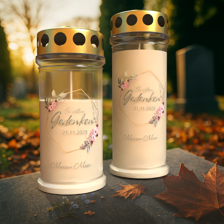 Personalisierte Gedenkkerze „In stillem Gedenken“ mit Name und Datum, Grablicht mit Blumenmotiv und goldenem Schutzdeckel auf Friedhof