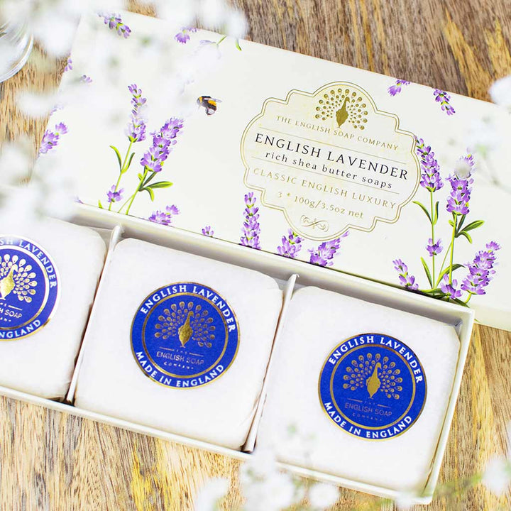 „Nahaufnahme einer Geschenkbox mit drei runden Seifen der Sorte ‘English Lavender’ auf Holzuntergrund, verziert mit Lavendelmotiv.“