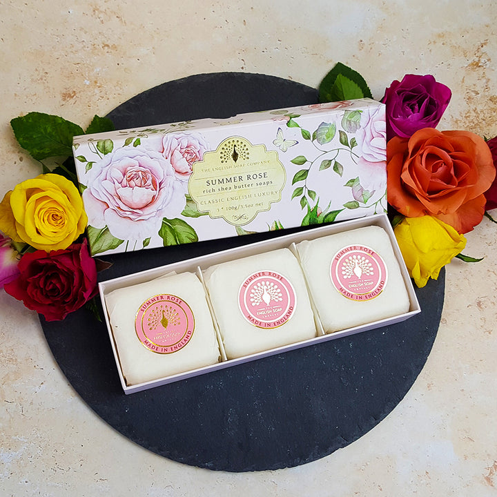 „Geschenkbox mit drei runden ‘Summer Rose’-Seifen auf schwarzem Untergrund, dekoriert mit bunten Rosenblüten in Gelb, Rot, Orange und Violett.“