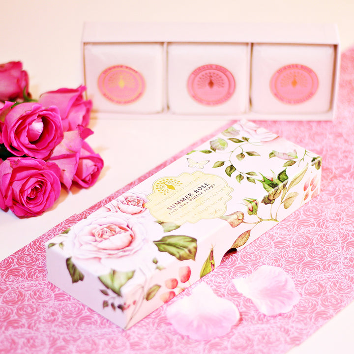„Geschenkbox mit drei ‘Summer Rose’-Seifen auf rosafarbenem Untergrund, dekoriert mit Rosenblüten und Rosenblättern.“