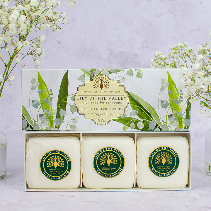 „Geschenkverpackung mit drei Seifenstücken der Sorte ‘Lily of the Valley’ in weiß-grüner Box mit floralem Design, aufrecht stehend, dekoriert mit Schleierkraut.“