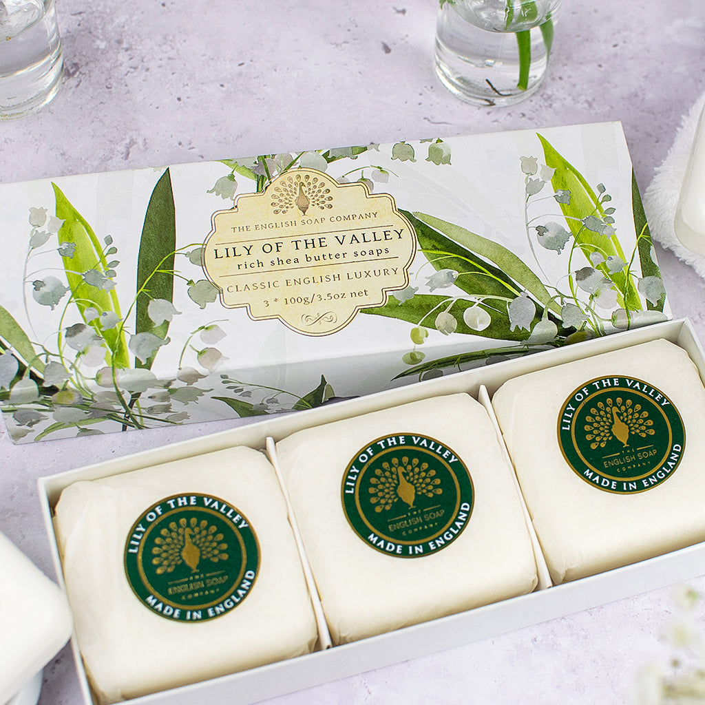 „Geschenkbox mit drei runden Seifenstücken der Sorte ‘Lily of the Valley’, einzeln verpackt und mit grünem Etikett, auf hellem Untergrund arrangiert.“