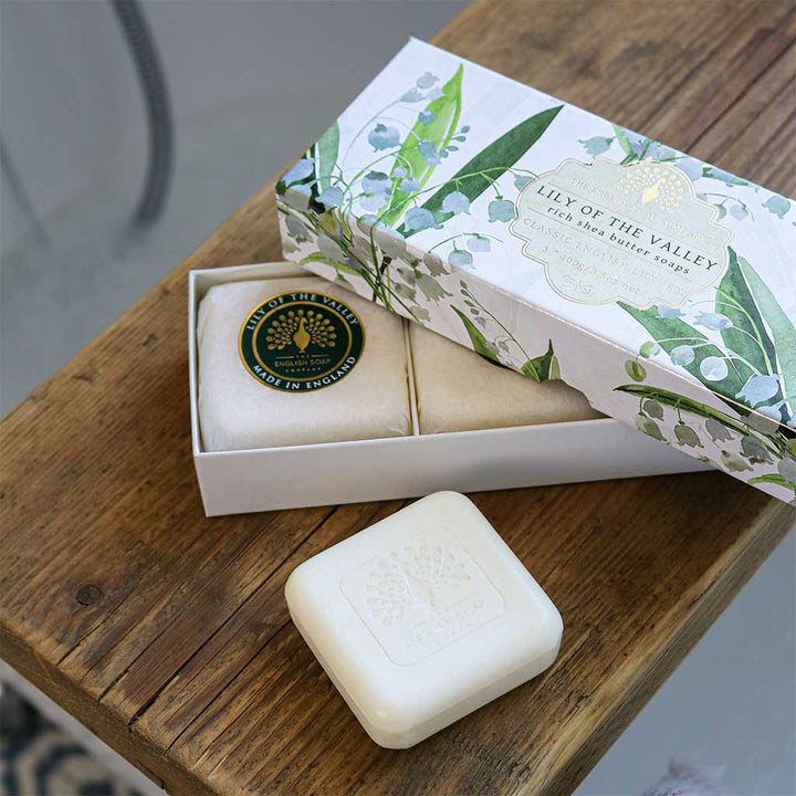 Geschenkbox mit drei runden Seifenstücken der Sorte ‘Lily of the Valley’, eine Seife liegt separat auf einem Holztisch.“