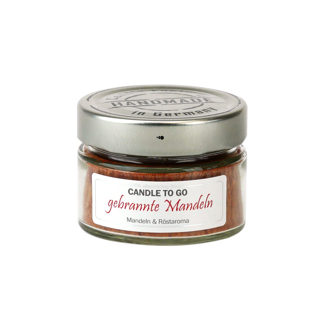 Kleine rote Duftkerze im Glas mit Metalldeckel und Etikett „Candle to go – gebrannte Mandeln“ auf weißem Hintergrund.