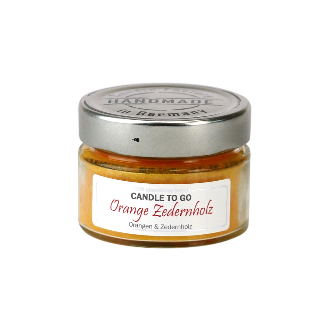 Kleine orange Duftkerze im Glas mit Metalldeckel und Etikett „Candle to go – Orange Zedernholz“ auf weißem Hintergrund.