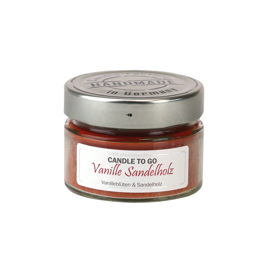 Kleine rote Duftkerze im Glas mit Metalldeckel und Etikett „Candle to go – Vanille Sandelholz“ auf weißem Hintergrund.