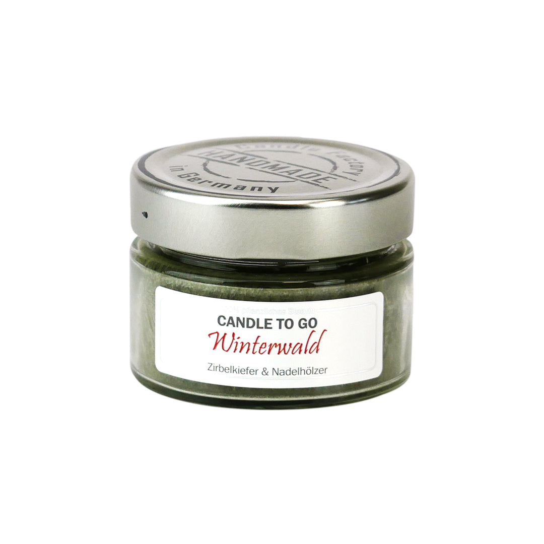 Kleine grüne Duftkerze im Glas mit Metalldeckel und Etikett „Candle to go – Winterwald“ auf weißem Hintergrund.