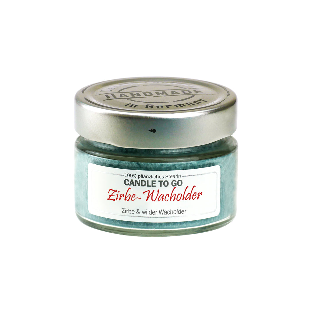 Kleine grüne Duftkerze im Glas mit Metalldeckel und Etikett „Candle to go – Zirbe-Wacholder“ auf weißem Hintergrund.