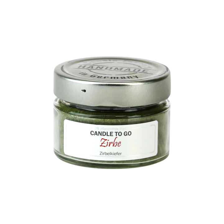 Kleine grüne Duftkerze im Glas mit Metalldeckel und Etikett „Candle to go – Zirbe“ auf weißem Hintergrund.