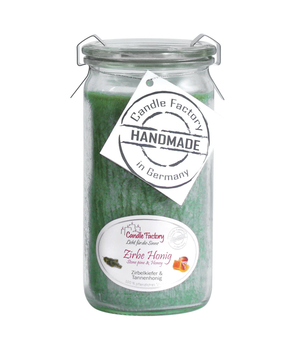 Grüne Duftkerze im hohen Glas mit Etiketten „Zirbe-Honig“ und „Handmade in Germany“ auf weißem Hintergrund.
