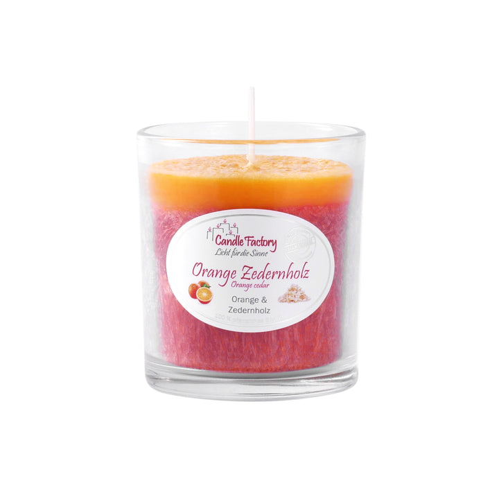 Duftkerze im Glas mit orange-roter Oberfläche und Etikett „Orange Zedernholz“, mittig platziert auf weißem Hintergrund.