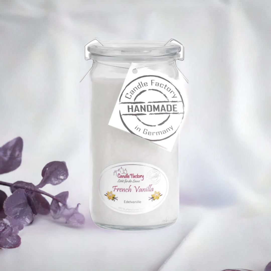 Weiße Duftkerze im Glas mit Etiketten „French Vanilla“ und „Handmade in Germany“, daneben violette Dekozweige.