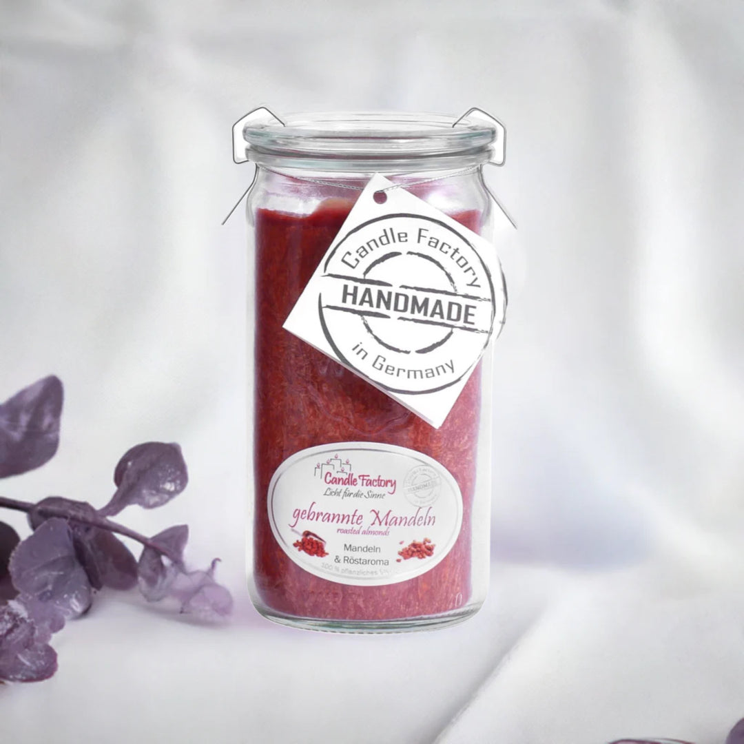 Rote Duftkerze im Glas mit Etiketten „Gebrannte Mandel“ und „Handmade in Germany“, daneben violette Dekozweige.