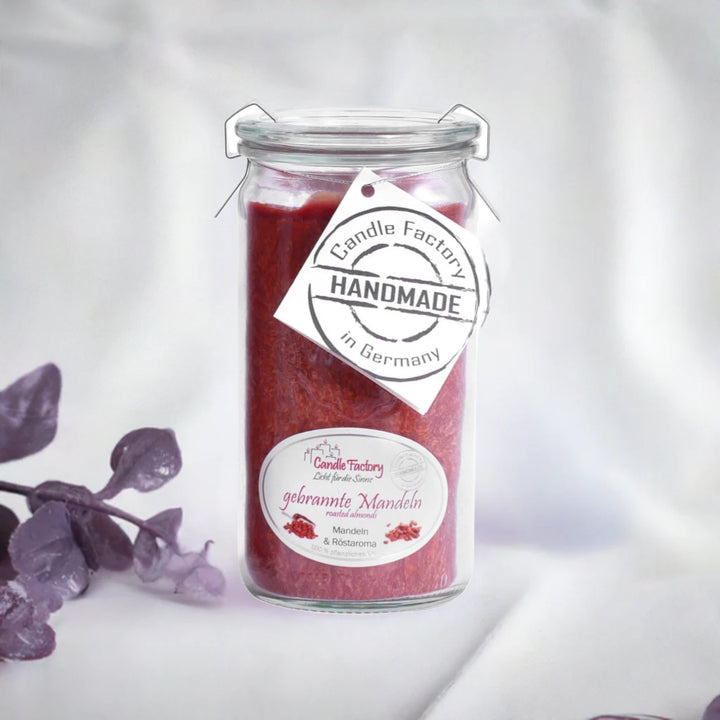 Rote Duftkerze im Glas mit Etiketten „Gebrannte Mandel“ und „Handmade in Germany“, daneben violette Dekozweige.