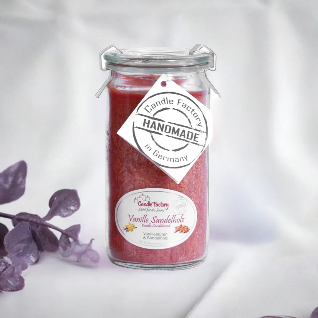 Rote Duftkerze im Glas mit Etiketten „Vanille Sandelholz“ und „Handmade in Germany“, daneben violette Dekozweige.