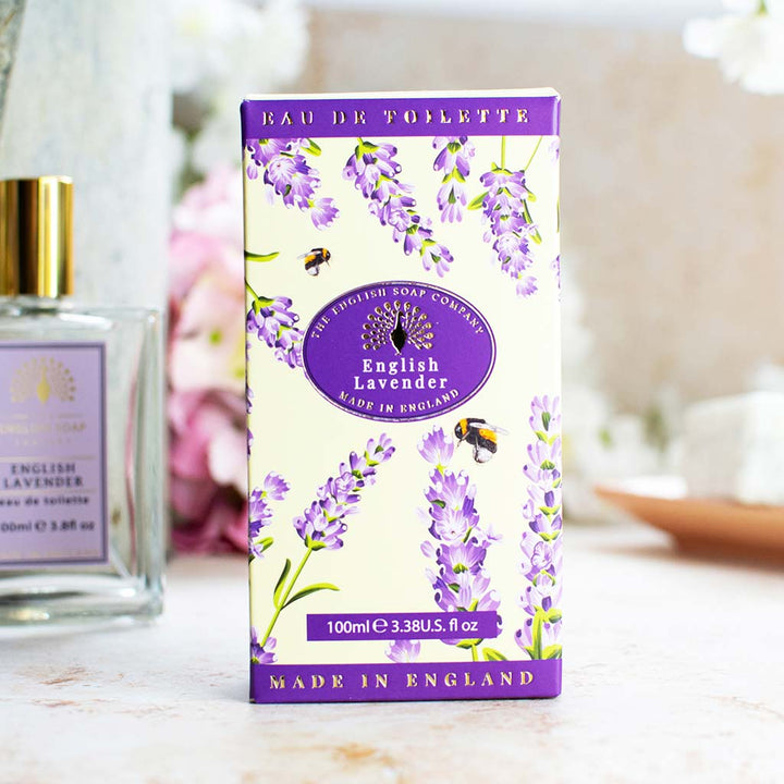 Verpackung der Eau de Toilette „English Lavender“ mit Lavendelblüten und Bienen, im Hintergrund teilweise sichtbare Glasflasche und Dekoration.