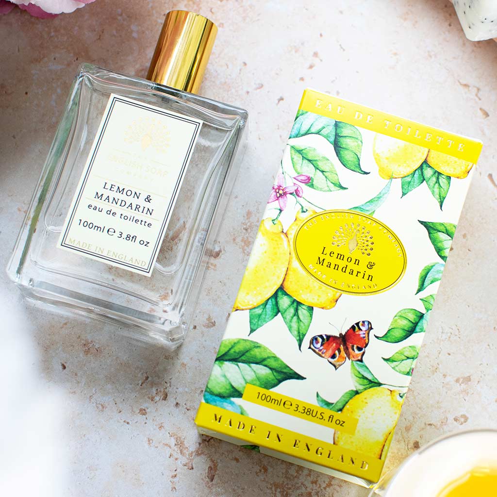 Glasflakon des Eau de Toilette Lemon &amp; Mandarin 100 ml mit goldener Kappe und Zitrusfrüchten im Hintergrund.