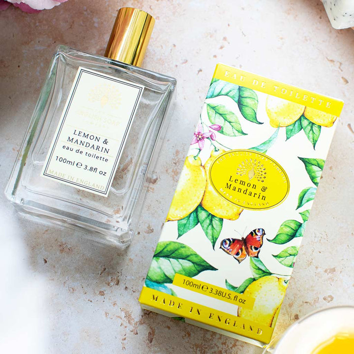 Glasflakon des Eau de Toilette Lemon &amp; Mandarin 100 ml mit goldener Kappe und Zitrusfrüchten im Hintergrund.