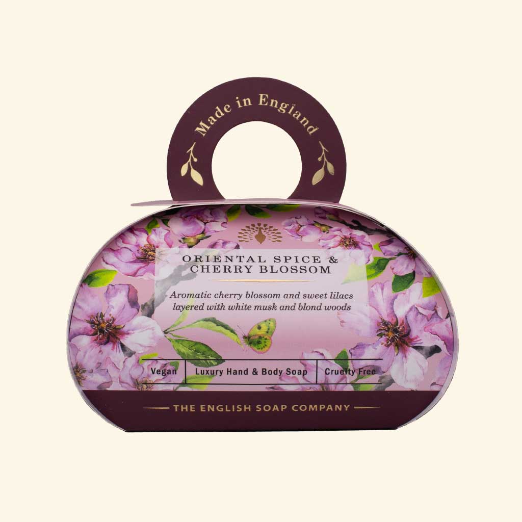 Luxus-Hand- und Körperseife der Marke The English Soap Company in ovaler Verpackung mit Tragegriff, Kirschblüten, Flieder und Blättern auf hellem Hintergrund, Aufschrift Oriental Spice & Cherry Blossom.