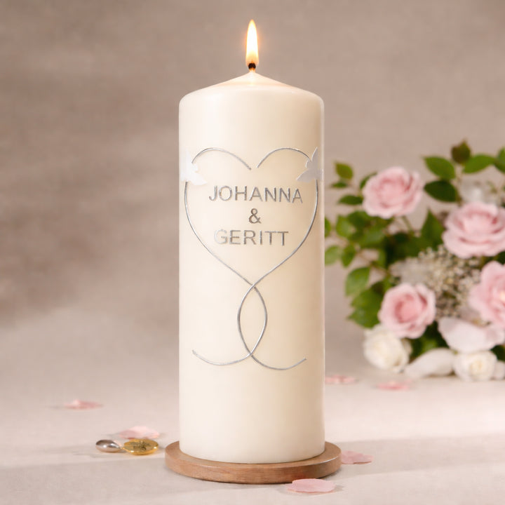 Romantische Hochzeitskerze in Elfenbein mit Taubenmotiv, dekoriert neben rosa Rosen auf Holzplatte im warmen Hintergrund