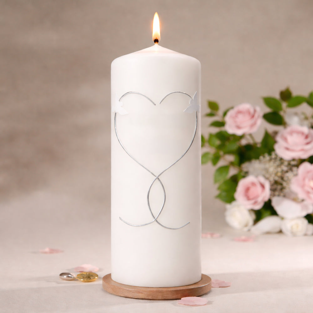 Detailaufnahme der Hochzeitskerze mit zwei weißen Tauben und silberner Wachslinie in Herzform auf elfenbeinfarbener Stumpenkerze