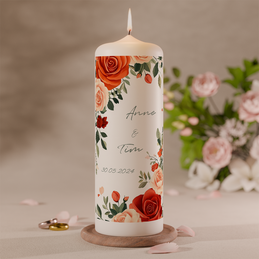 personalisierte hochzeitskerze mit rosenmotiv und namen des brautpaares auf weisser stumpenkerze mit brennender flamme