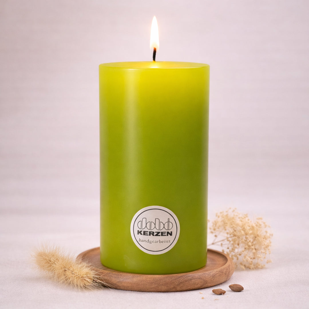 Lindgrüne Stumpenkerze handgefertigt von DOBO mit brennender Flamme auf Holzuntersetzer