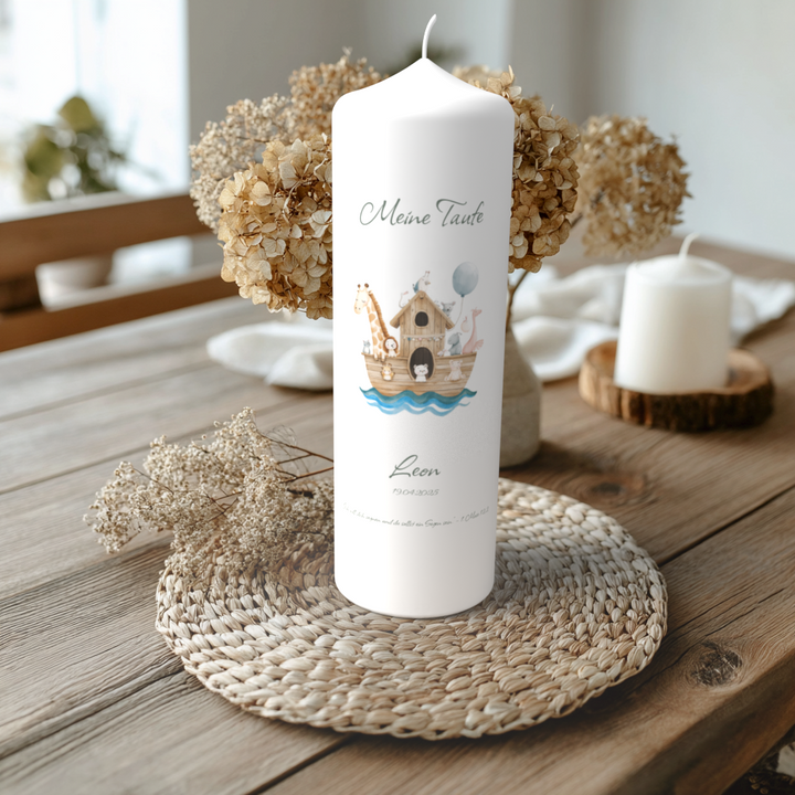 Handgefertigte Taufkerze mit Arche-Noah-Motiv, Name Leon, auf Holztisch mit Trockenblumen, liebevoll dekoriert.