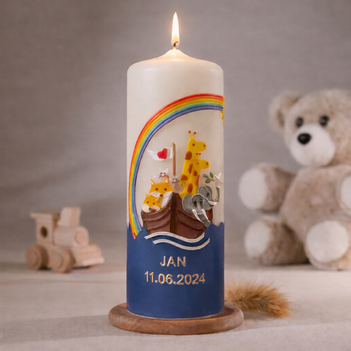 Weiße Taufkerze mit Arche Noah, Regenbogen und Tieren sowie personalisiertem Namen und Datum, stehend auf Holzsockel vor neutralem Hintergrund mit Teddybär