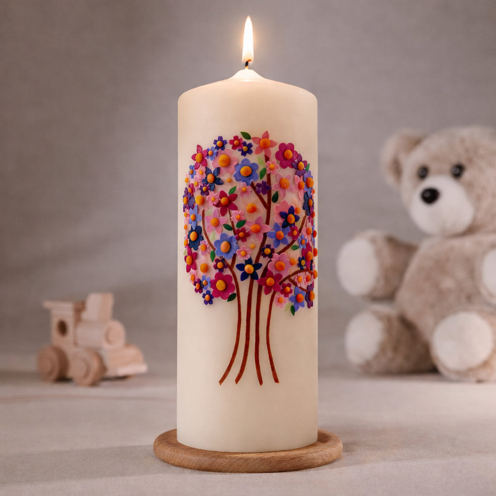 Cremefarbene Taufkerze mit buntem Baum des Lebens aus farbigen Blüten und roten Stämmen, brennend auf Holzsockel vor neutralem Hintergrund mit Teddybär
