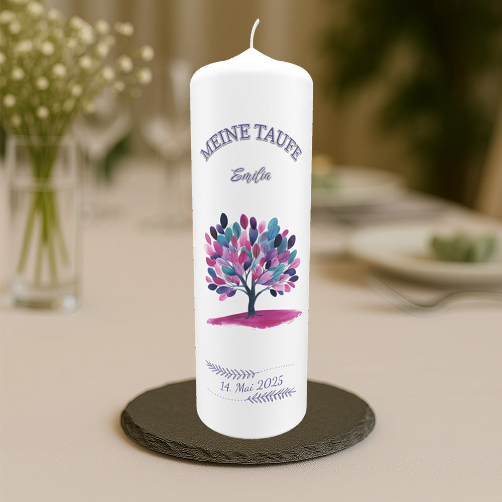 Weiße Taufkerze mit buntem Baum-Motiv, dem Schriftzug „Meine Taufe“, dem Namen „Emilia“ und dem Taufdatum „14. Mai 2025“, arrangiert auf einem Tisch mit unscharfem Hintergrund.