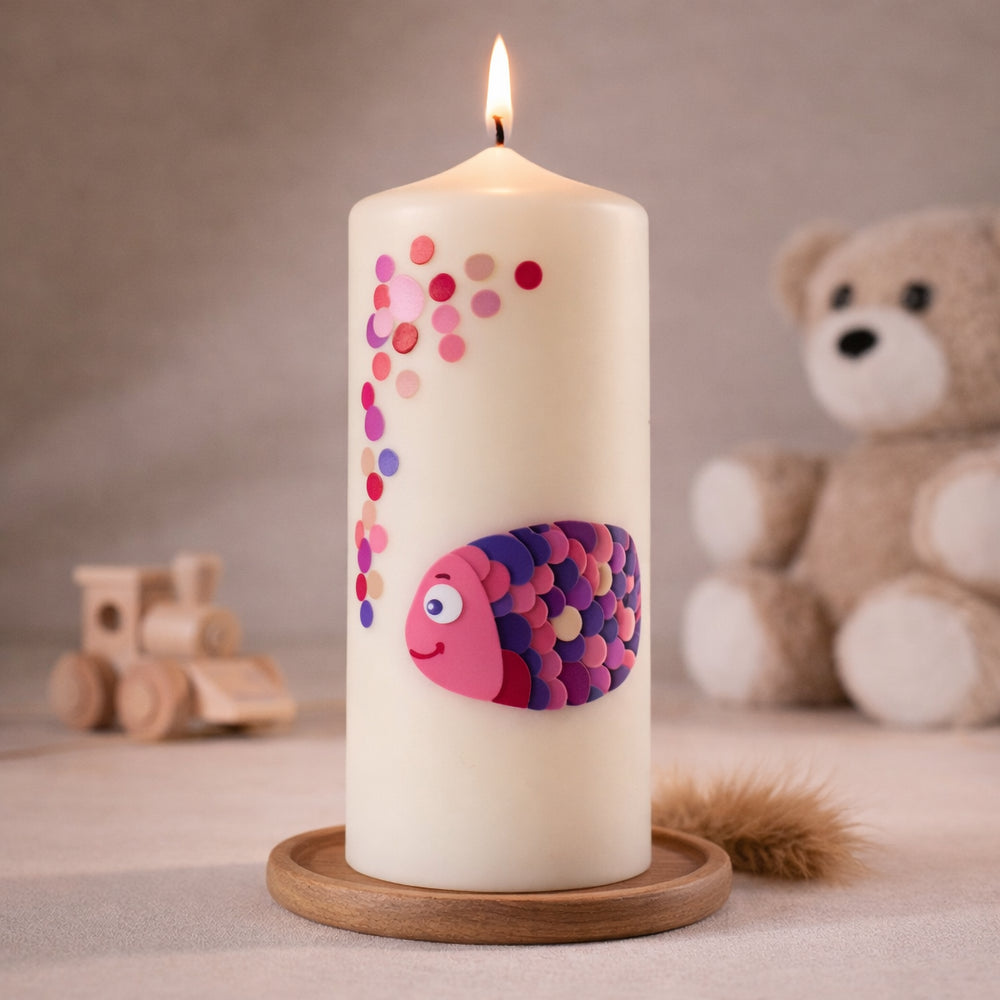 elfenbeinfarbene Taufkerze mit rosa-lila Fischmotiv und Punkten, stehend auf Holzsockel vor neutralem Hintergrund mit Teddybär