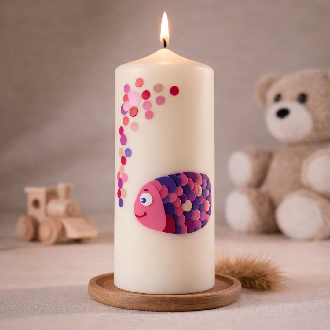 elfenbeinfarbene Taufkerze mit rosa-lila Fischmotiv und Punkten, stehend auf Holzsockel vor neutralem Hintergrund mit Teddybär