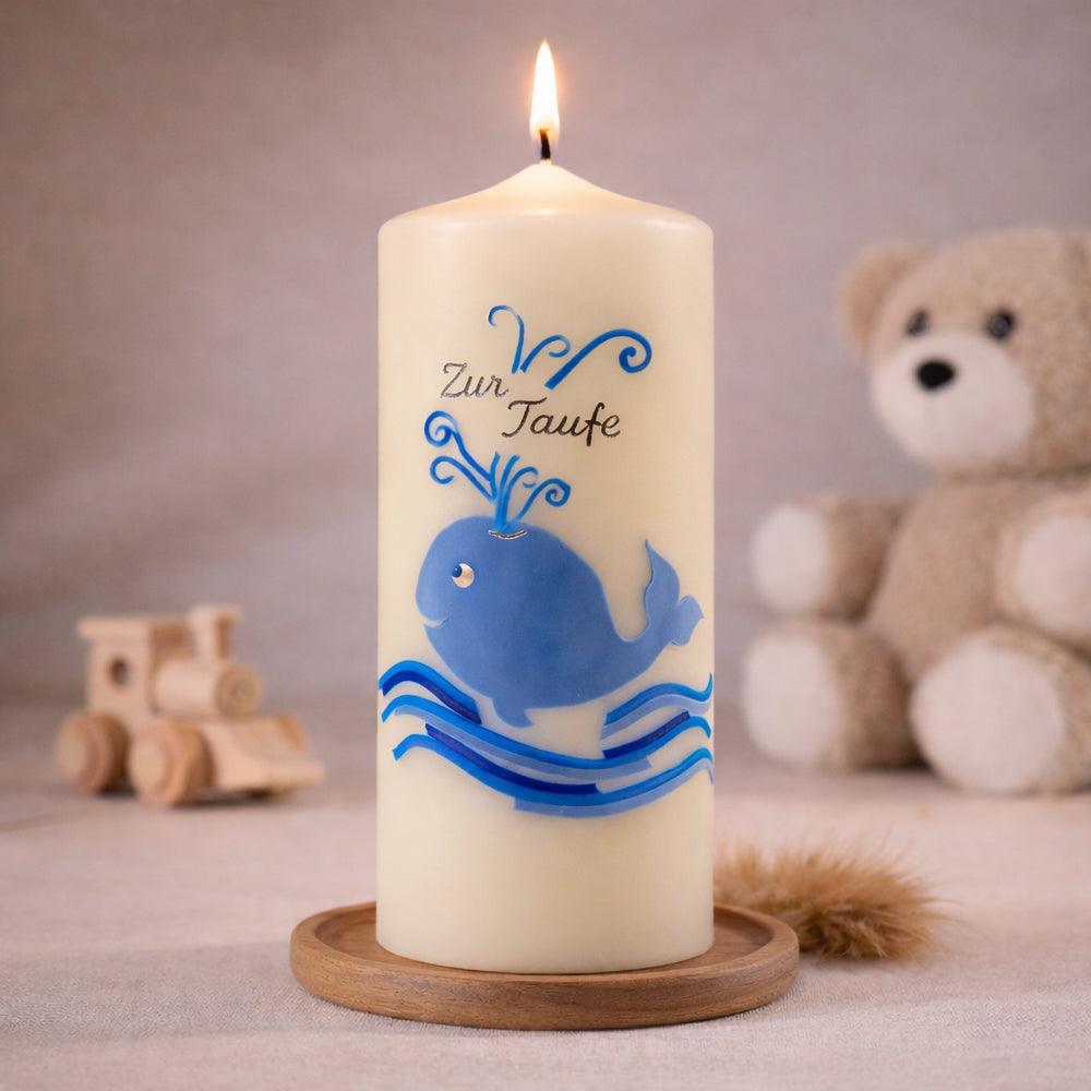 elfenbeinfarbene Taufkerze mit blauem Wal und Wellen, stehend auf Holzsockel vor neutralem Hintergrund mit Teddybär