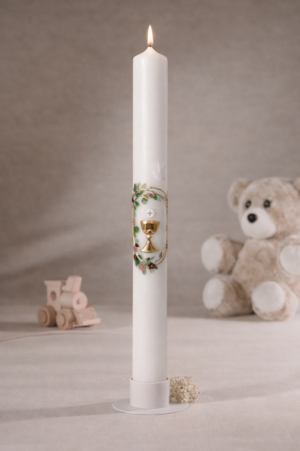 
Weiße Taufkerze mit Kelchmotiv, goldfarbenem Kreuz, grünen Ranken und Taube, stehend auf Kerzenteller vor neutralem Hintergrund mit Teddybär und Holzspielzeug
