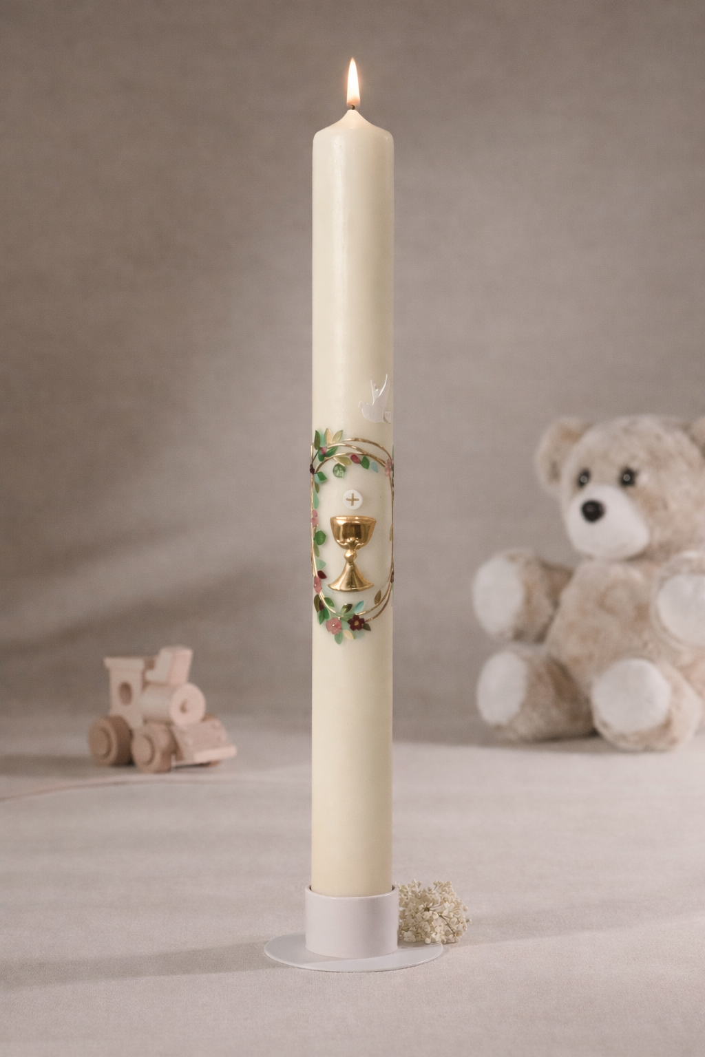 Schmale Taufkerze mit Kelchmotiv, goldfarbenem Kreuz, grünen Ranken und weißer Taube, fotografiert vor neutralem Hintergrund mit Teddybär und Holzspielzeug

