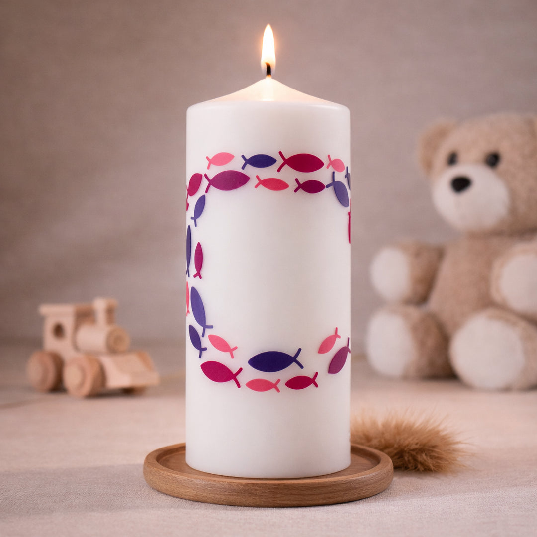 Weiße Taufkerze mit Fischsymbolen im Kreis in Rosa und Lila, brennend auf Holzsockel vor neutralem Hintergrund mit Teddybär