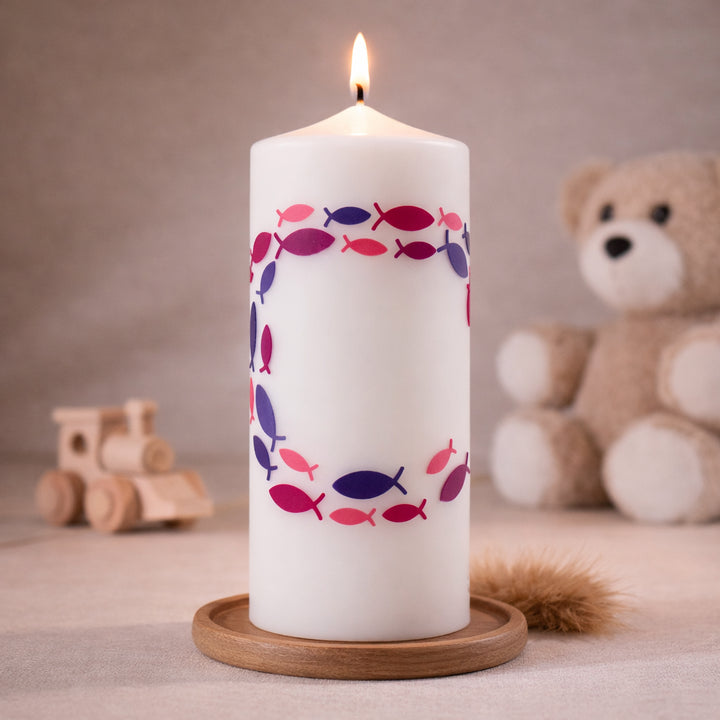 Weiße Taufkerze mit Fischsymbolen im Kreis in Rosa und Lila, brennend auf Holzsockel vor neutralem Hintergrund mit Teddybär